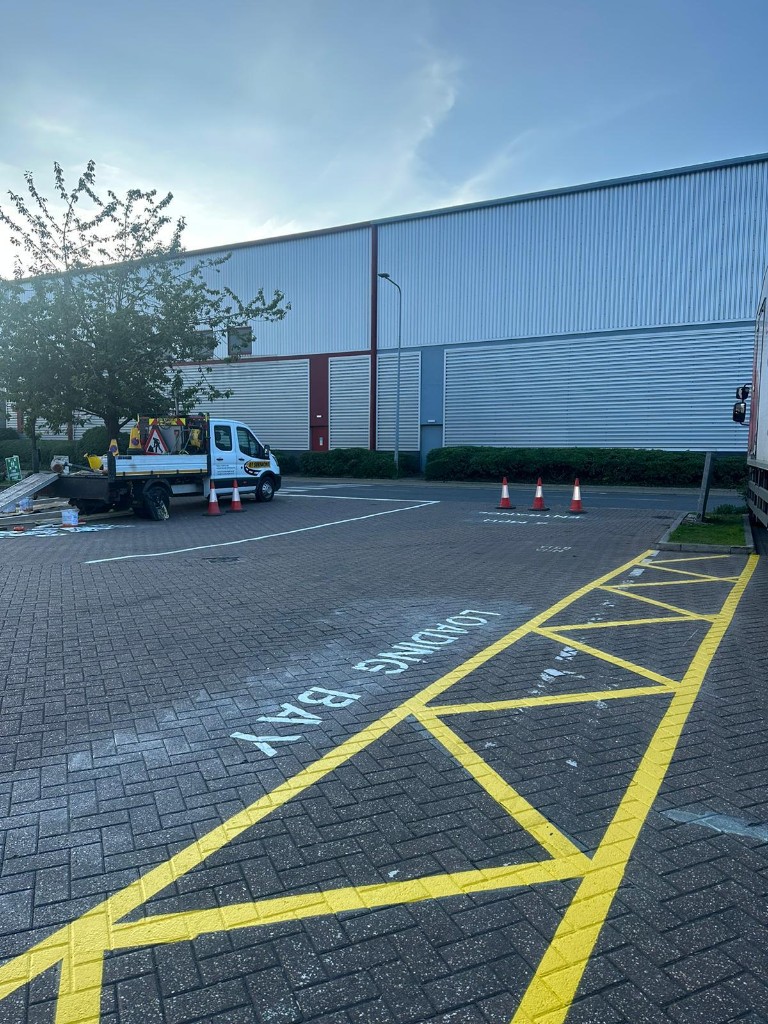 Loading bay words and yellow hatched keep-clear zone painted on block paving at an industrial site