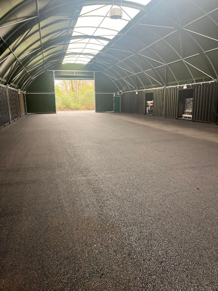 Interior of a large arched warehouse with new grey asphalt floor and skylit roof