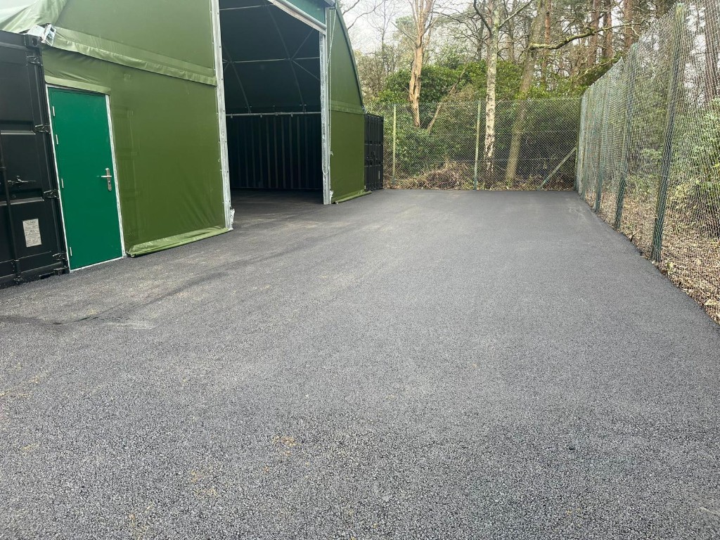 Fresh asphalt yard surface beside a green industrial canopy building