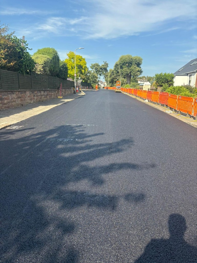 Estate road with new asphalt, orange safety barriers and roller in the distance