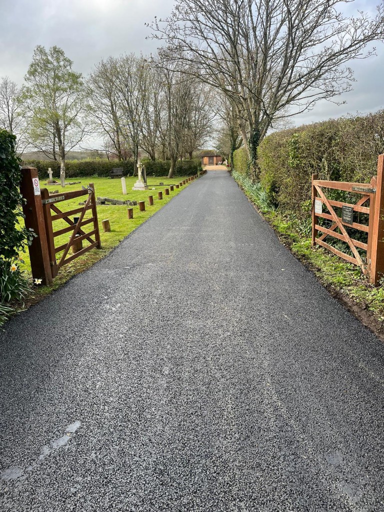 Asphalt access route through entrance gates alongside memorial lawns
