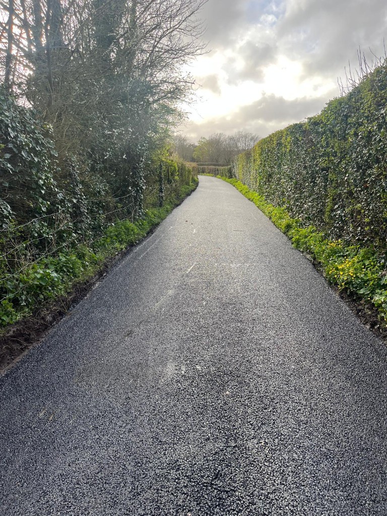 Fresh asphalt on a long rural access road between hedges