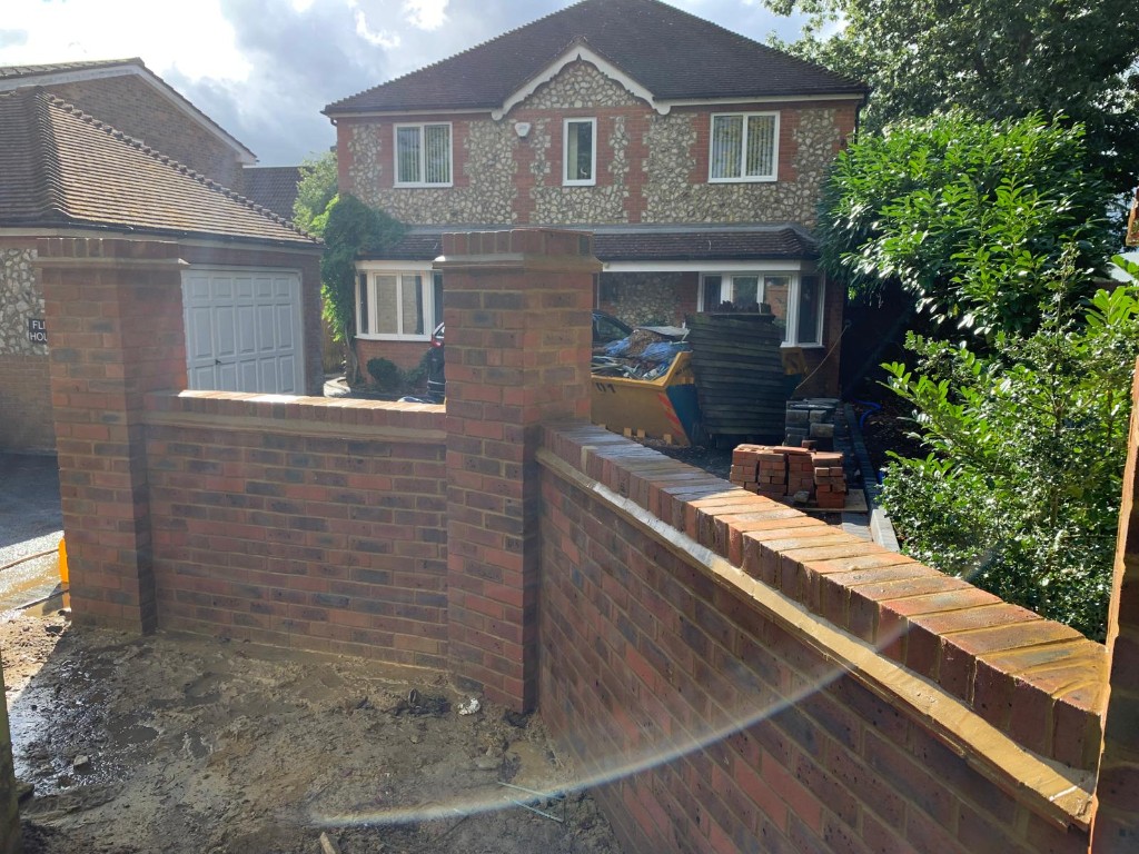 Tall brick pillars with coping at a driveway entrance beside a wooden fence