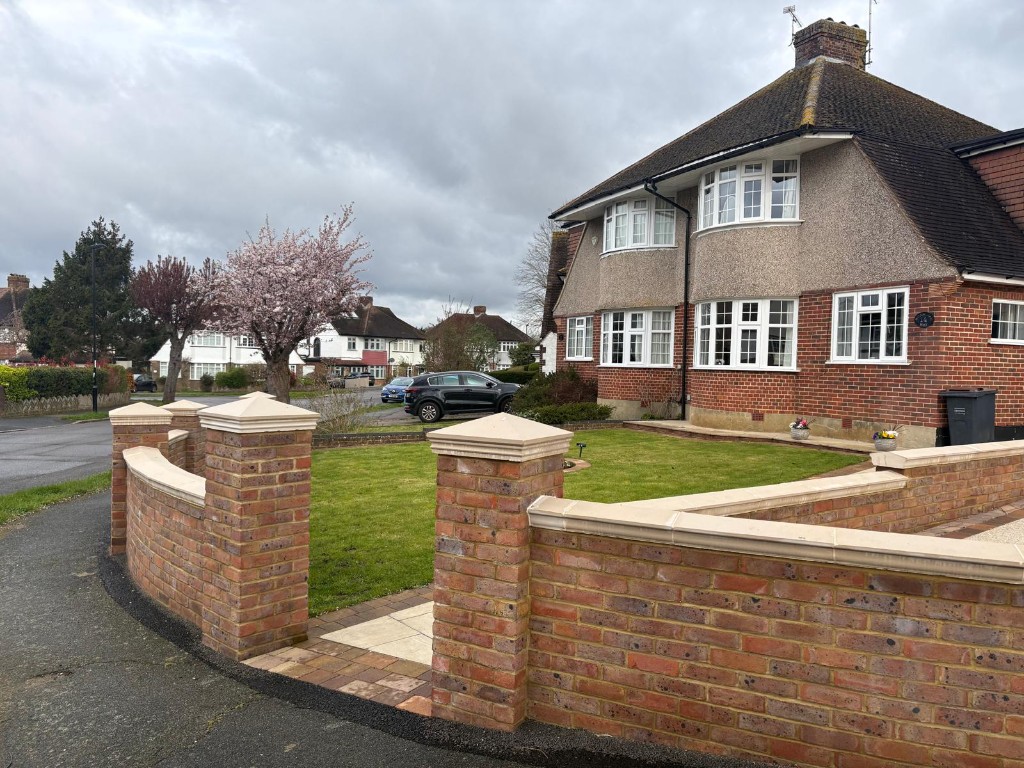 Curved multi-tone brick front wall with stone-capped piers, flat coping and paved entrance opening