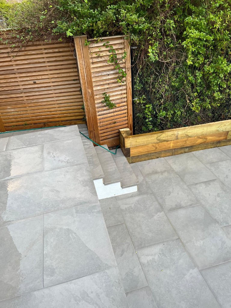 Natural stone patio leading to a grey garden room with full-height glass and dark fence