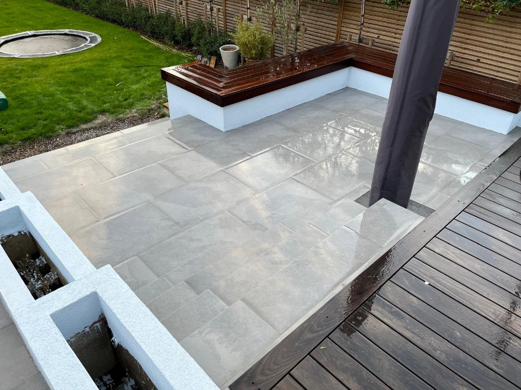 Rear garden patio with grey stone slabs, built-in bench seating and slatted timber fence