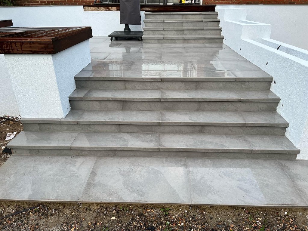 Multi-level outdoor terrace in large grey tiles with white rendered planters and timber details