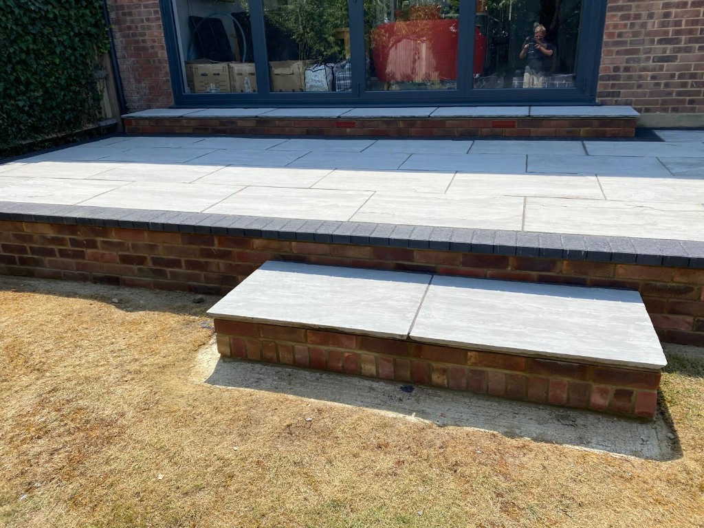 Raised terrace flush to bifolding doors with brick retaining wall and lawn transition