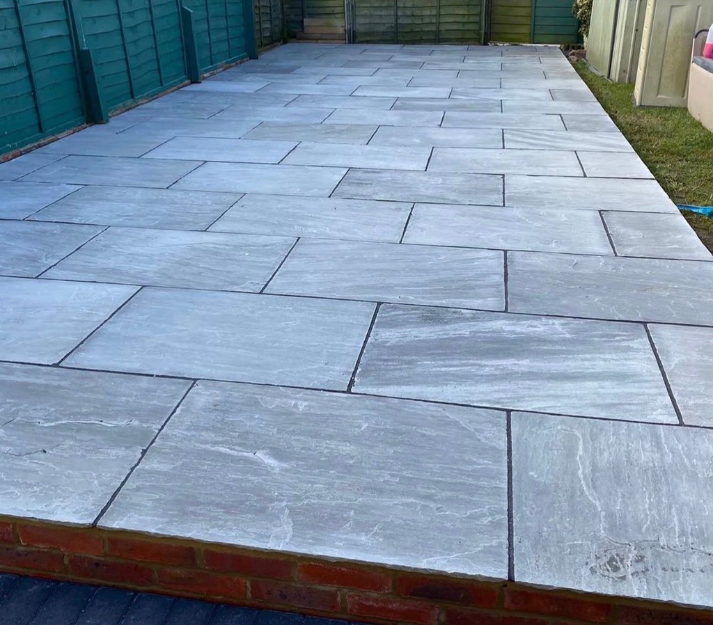 Large grey natural stone patio in stretcher bond with dark joints, timber fence and lawn beyond