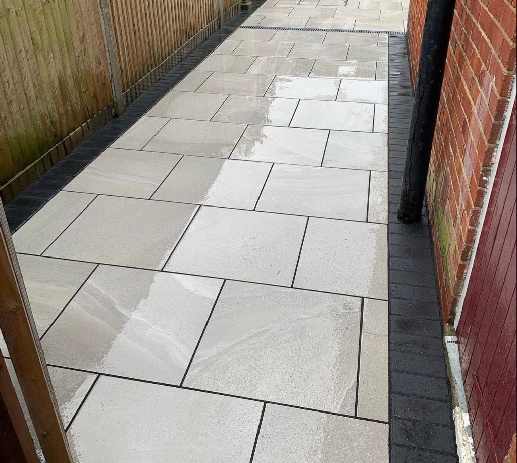 Garden path paved with large light stone slabs and dark block border beside timber fence and brick house wall