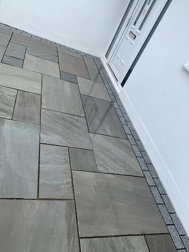 Polished grey paving slabs with dark square sett border against brick walls