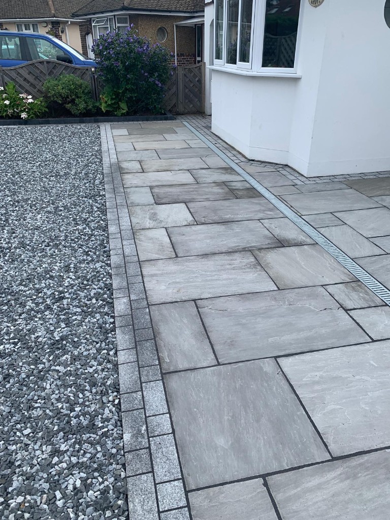 Diagonal view of buff and grey natural stone paving toward a white front door