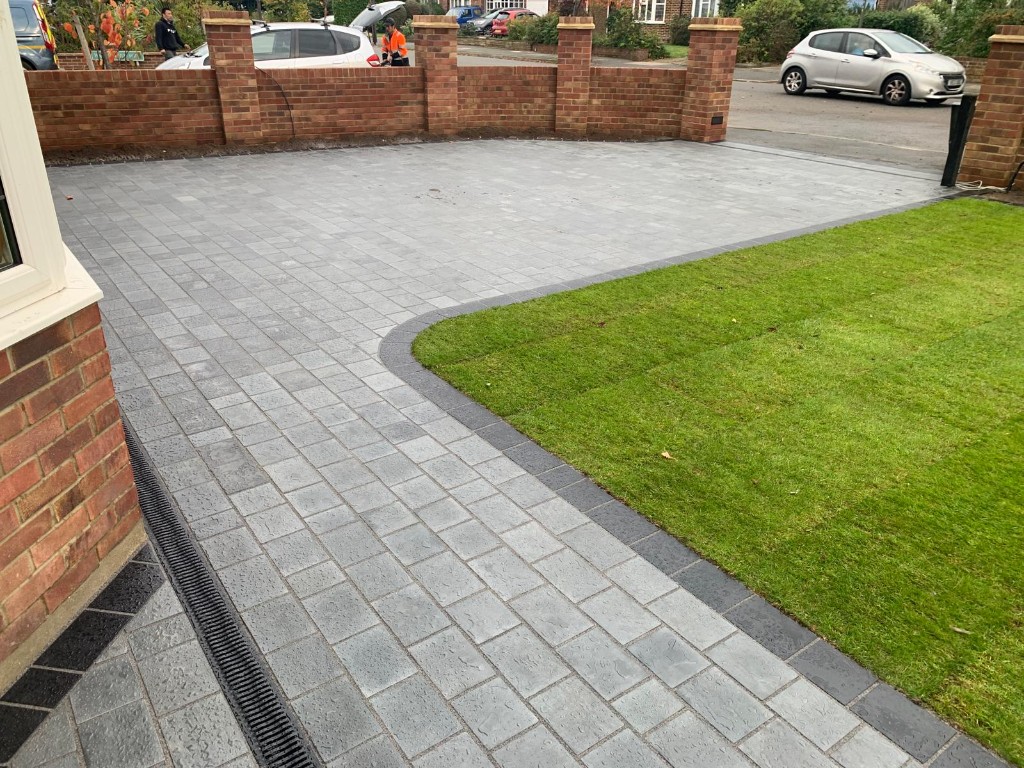 Grey block paved driveway with dark border, lawn and linear drainage by the house
