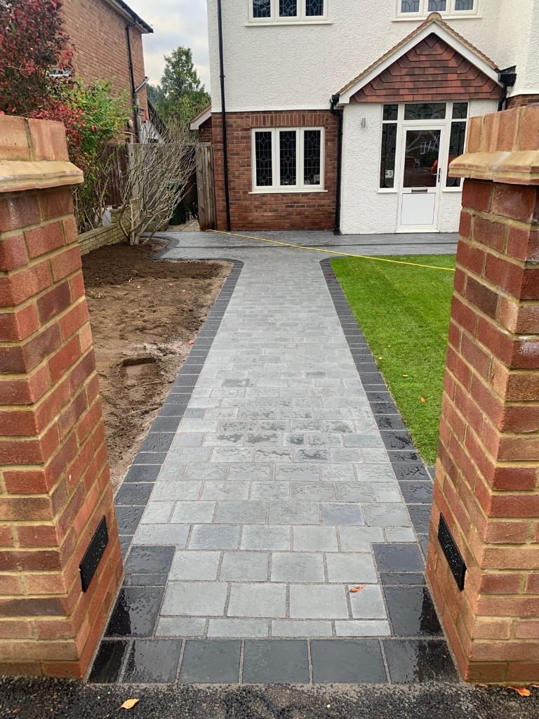 Grey paved path and driveway from brick entrance pillars to a traditional house front door