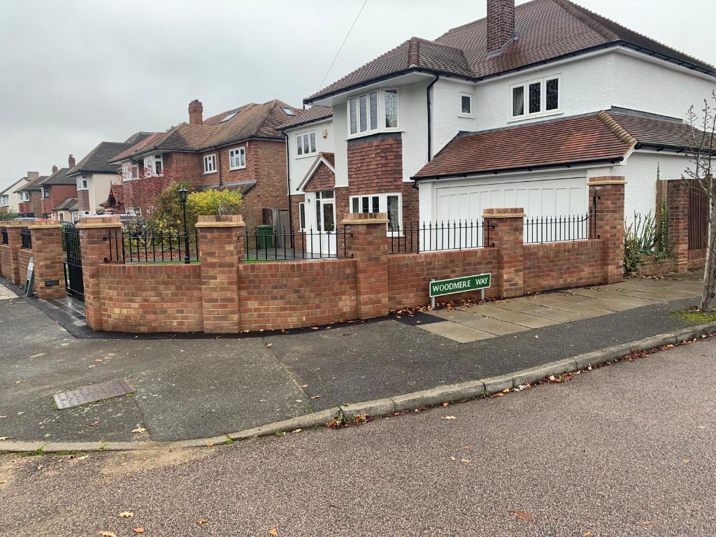 Corner property with curved brick boundary wall, stone-capped pillars and metal railings
