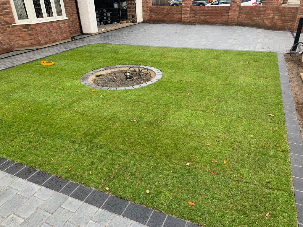 Overhead view of new turf lawn surrounded by grey block paving with circular paved feature
